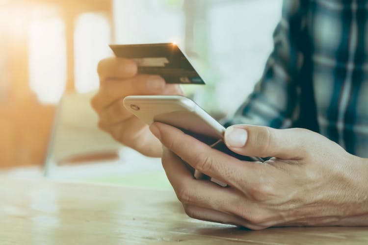 A person holds a credit card above a mobile phone.